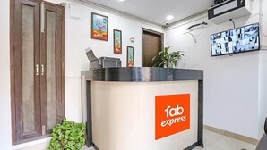 A reception desk with a 'fab express' sign, a potted plant, and a security camera on the wall. - Fabexpress Premium Room I (New Delhi)