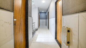 A corridor with wooden doors and white walls, leading to a room with a bed. - Fabhotel Unity Landmark (Indore)