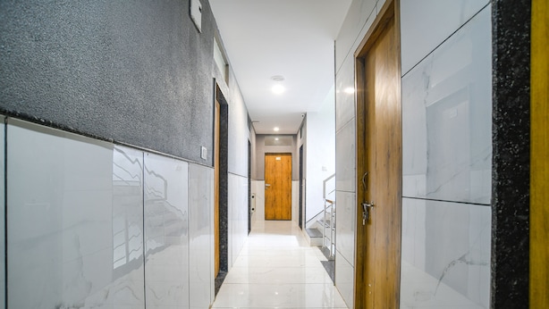 A hallway with marble walls, a wooden door at the end, and a tiled floor. - Fabhotel Unity Landmark (Indore)