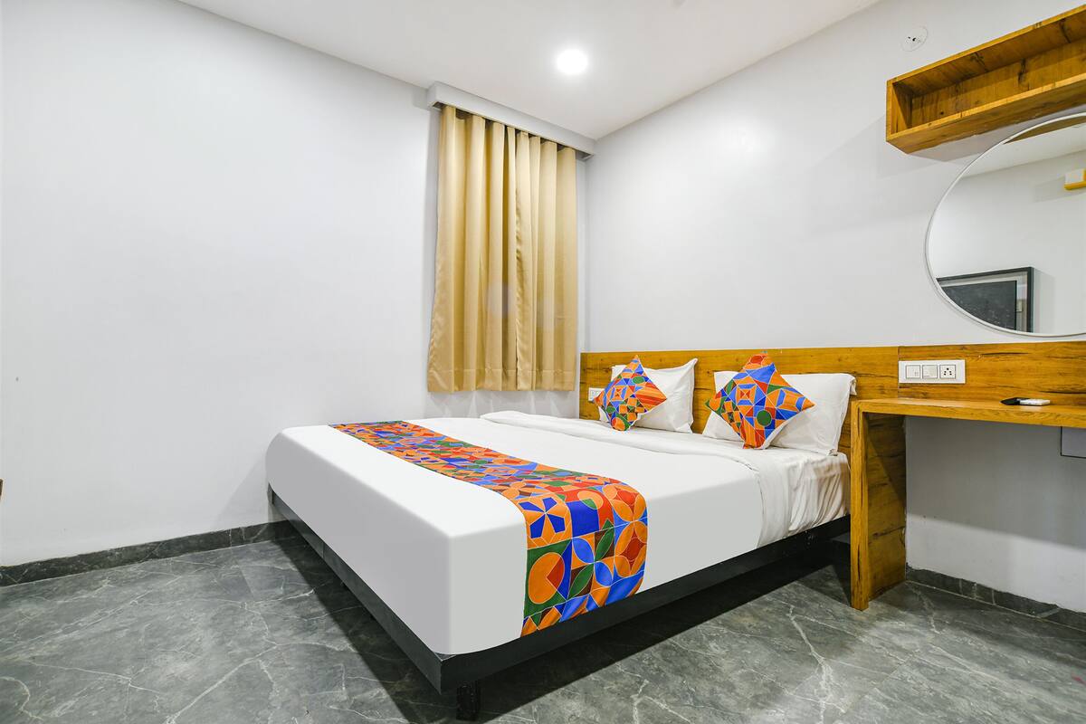 A hotel room with a bed, a desk, a mirror, and a window with curtains.