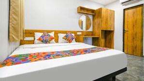 A neatly made bed with a colorful geometric-patterned bedspread, a wooden headboard, a round mirror, and a wooden wardrobe. - Fabhotel Unity Landmark (Indore)