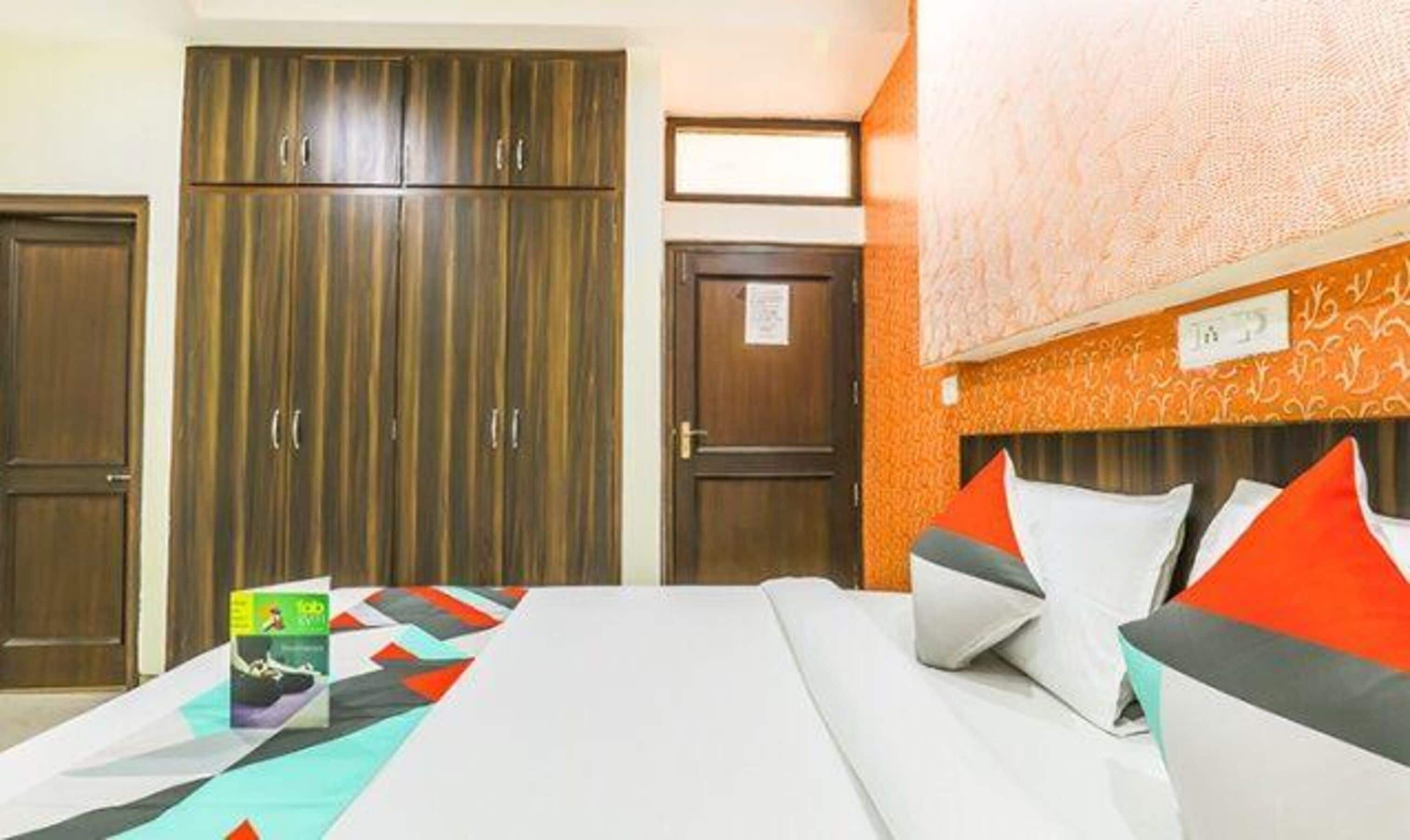 A hotel room with a large wardrobe, a bed with colorful bedding, and a patterned wall.