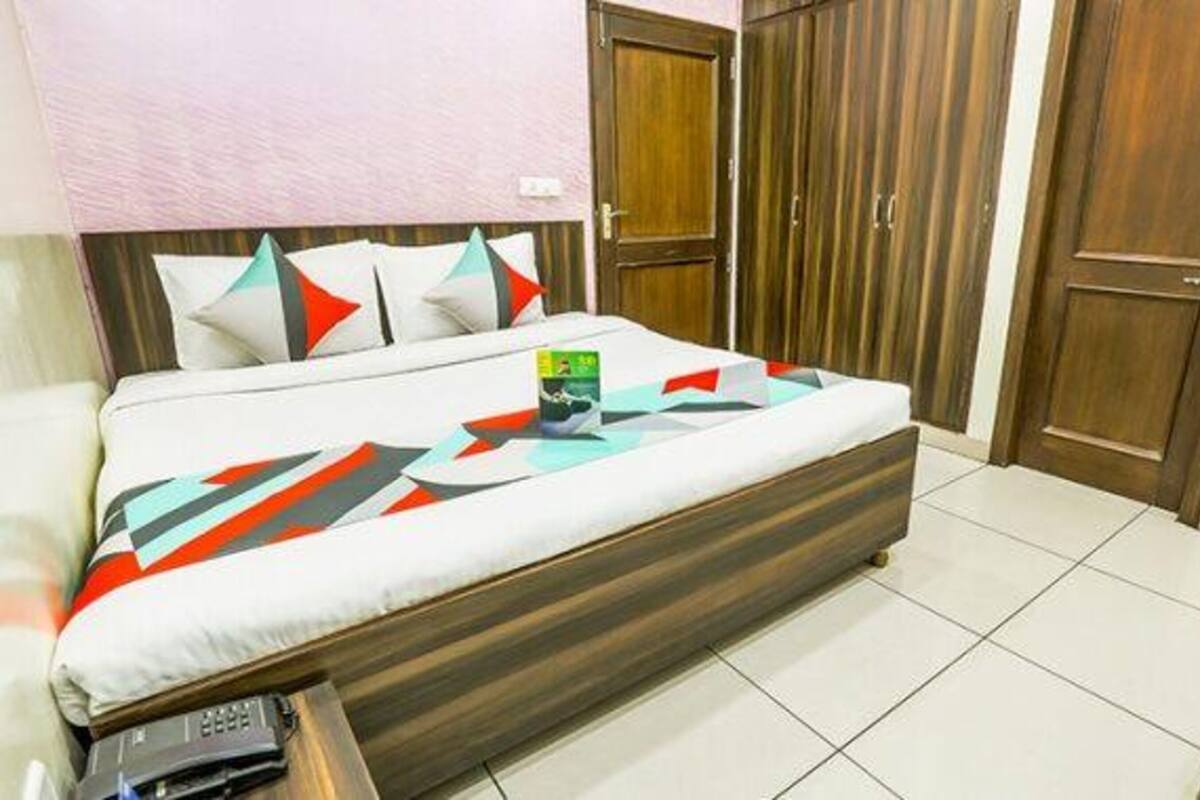 A neatly made bed with a patterned bedspread, a bedside table with a book, and a wooden wardrobe with two doors.