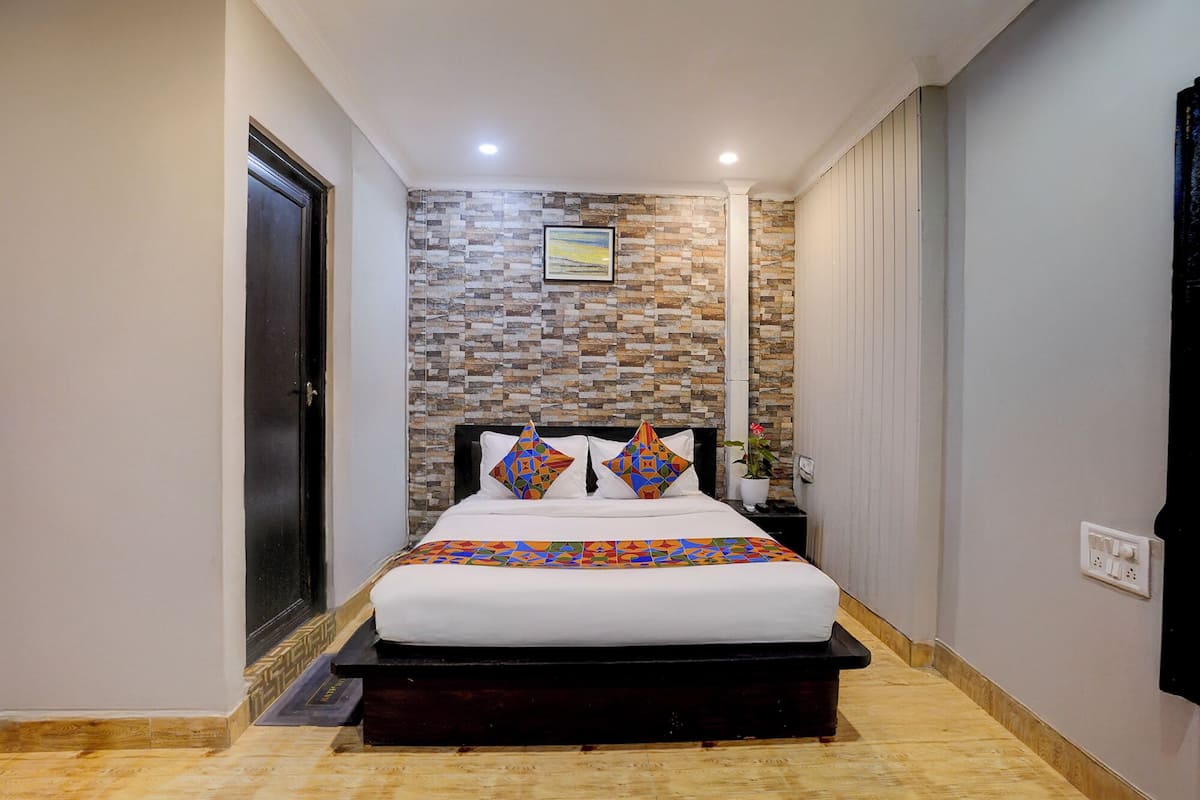 A bedroom with a stone-patterned wall, a bed with a colorful geometric bedspread, and a nightstand with a potted plant.