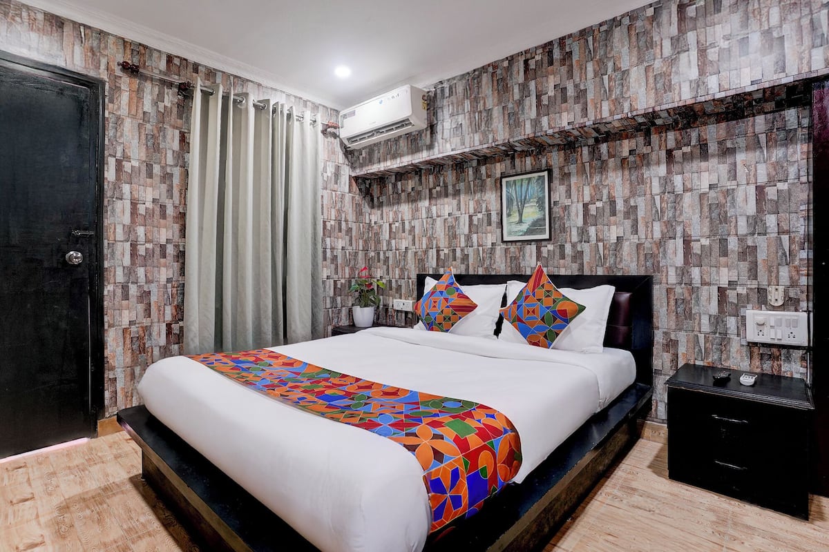 A bedroom with a bed, curtains, a nightstand, and a wall-mounted air conditioner.