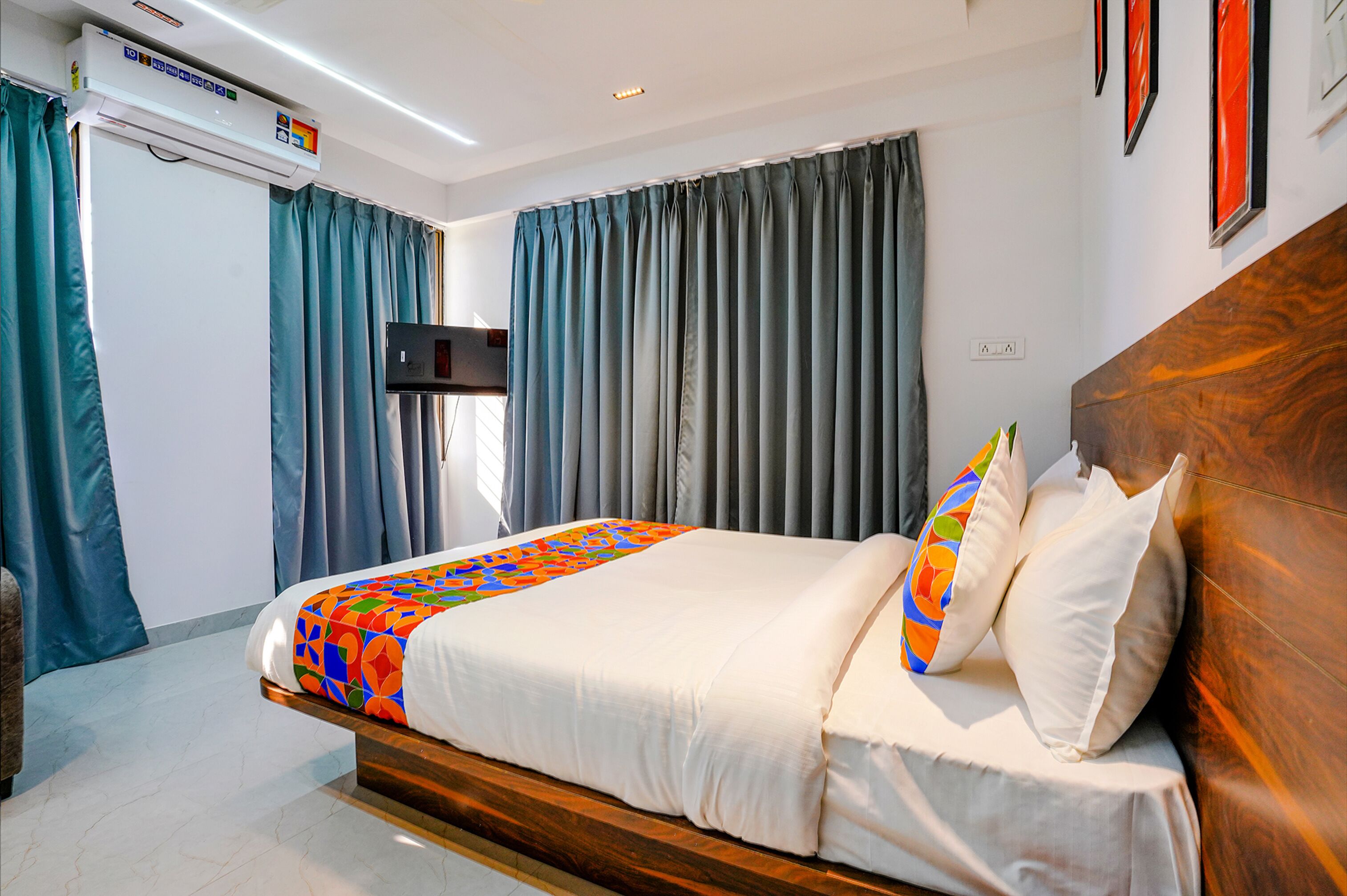 A hotel room with a bed, curtains, a mounted TV, and a wooden headboard.