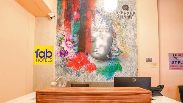 Una reception con un murale raffigurante Buddha, un cartello 'fab hotels', un computer Dell e un'insegna 'Le Grand'.