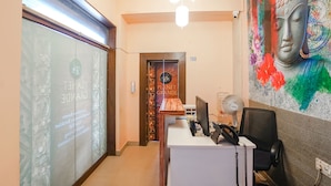 Una zona reception con scrivania, un computer, un telefono e una ventola a muro. Sulla parete, un grande murale raffigurante Buddha e un cartello con la scritta "Planet Grande".