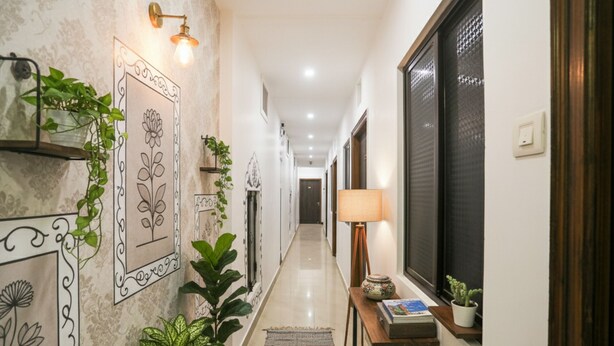 Un couloir doté d’un sol carrelé, de décorations murales, de plantes en pot, d’une lampe et d’une petite table sur laquelle se trouvent un livre et un vase.