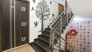 Un escalier avec une rampe en métal, une porte en bois avec une plaque numérotée et un mur décoré d’un motif représentant un arbre et un oiseau.