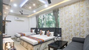 Une chambre d’hôtel avec deux lits, un canapé, une table basse, un ventilateur de plafond et de grandes fenêtres avec des rideaux.