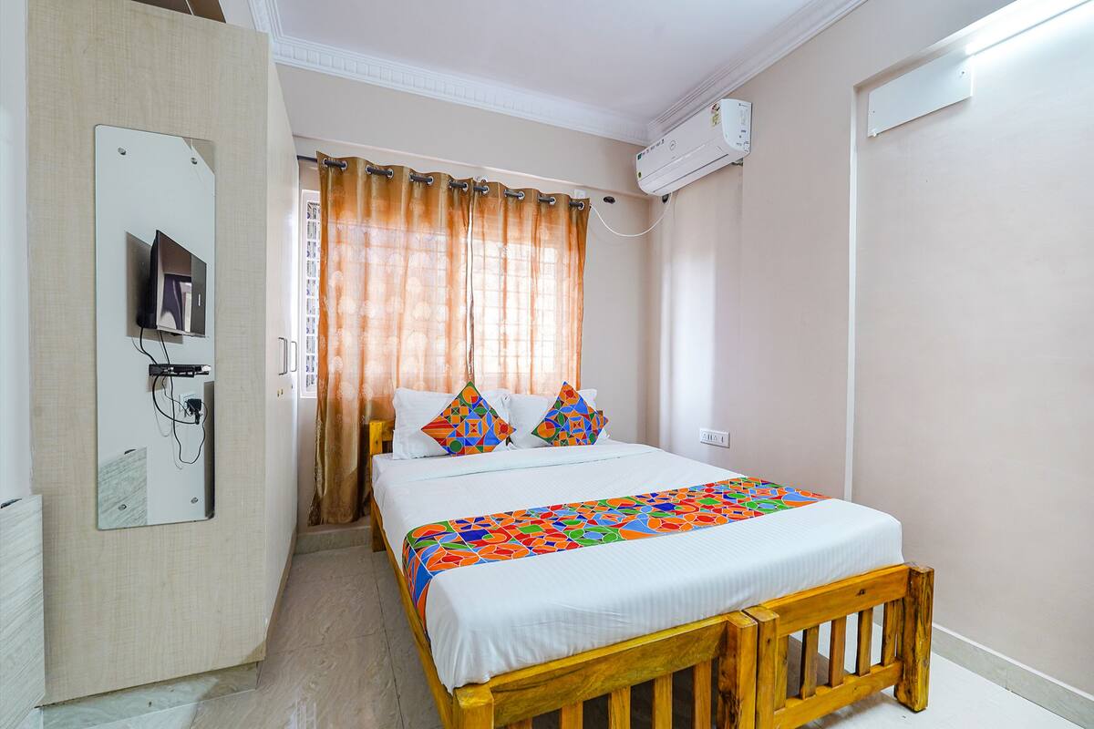 A bedroom with a bed, curtains, a TV mounted on the wall, and an air conditioning unit.