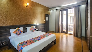 Une chambre d’hôtel dotée d’un grand lit, d’une tête de lit, d’une table de chevet, d’une lampe fixée au mur et d’une porte-fenêtre coulissante donnant sur un balcon.