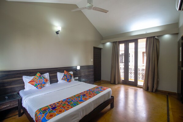 A hotel room with a bed, a nightstand, a ceiling fan, and a view of the outside balcony. - iNDO Homtel (Saligao)