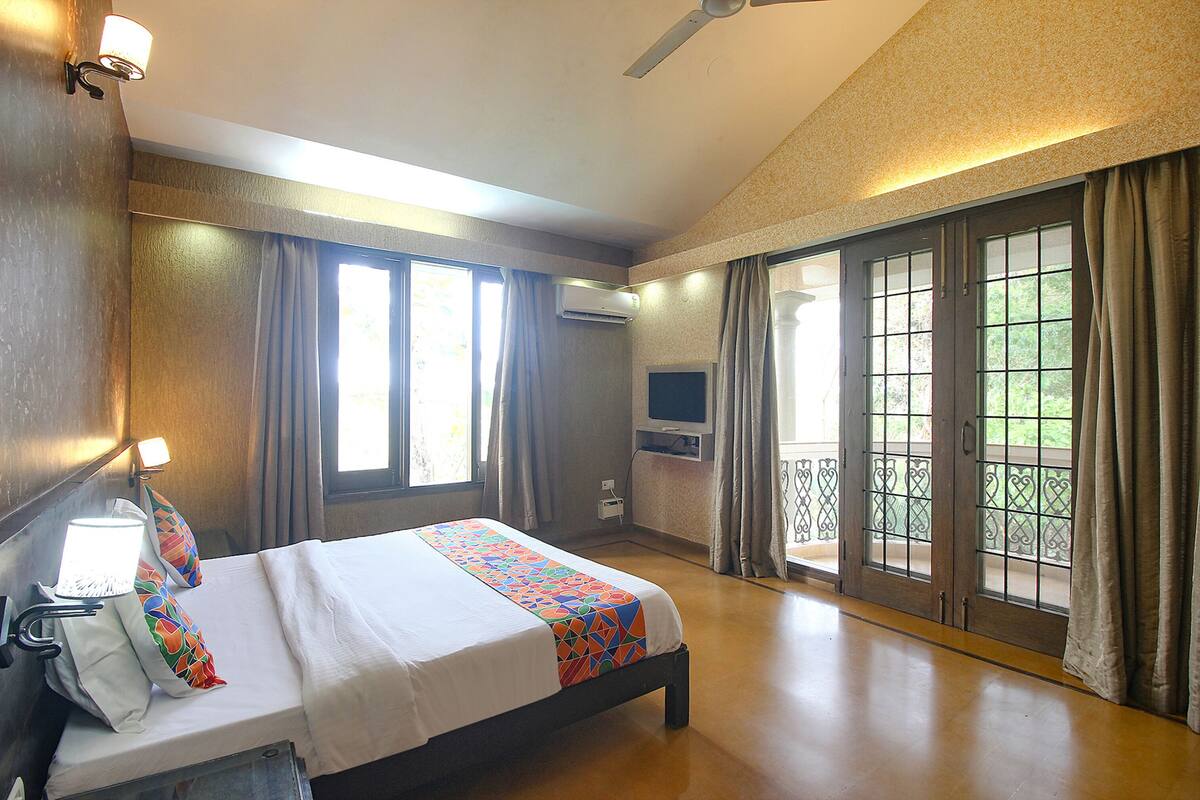 Une chambre d’hôtel équipée d’un lit, d’une télévision, d’un système de climatisation et d’un balcon avec des rideaux.