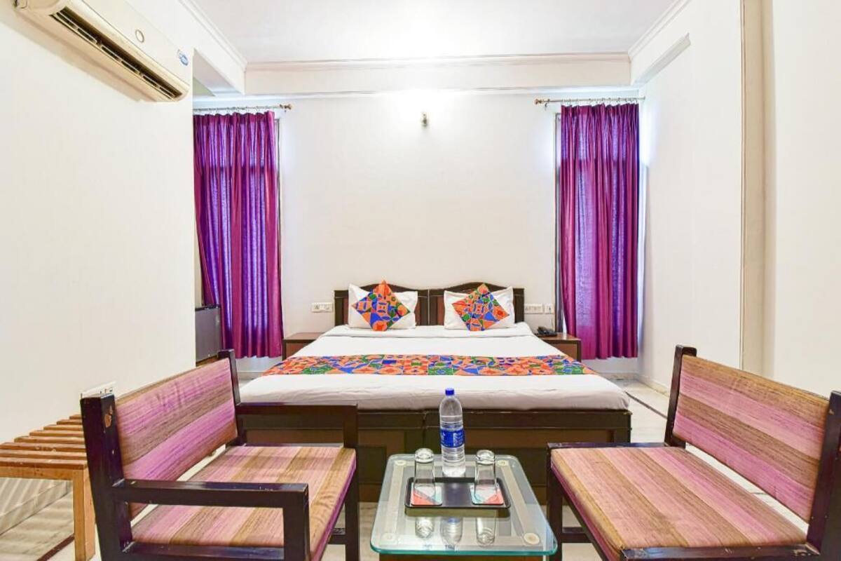 Hotelkamer met een bed, twee stoelen, een klein tafeltje met een waterfles en een raam met paarse gordijnen.
