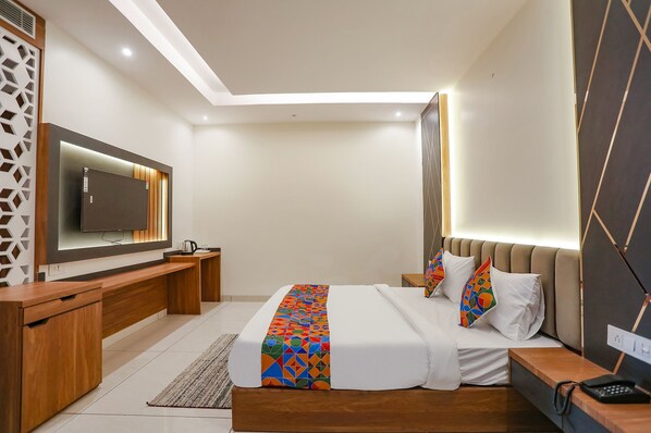 A modern hotel room with a large bed, wooden furniture, a flat-screen TV, and a bedside table with a phone. - FabHotel Royal 116 (Noida)