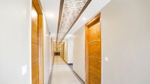 A long, narrow hallway with wooden doors on both sides and a patterned ceiling. - FabHotel Royal 116 (Noida)