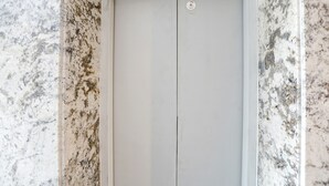 A closed elevator door with a control panel above it, set against a marble wall. - FabHotel Royal 116 (Noida)