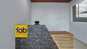 A reception desk with a 'fab hotels' sign, a wooden slatted bench, and a window with metal bars. - FabHotel Royal 116 (Noida)