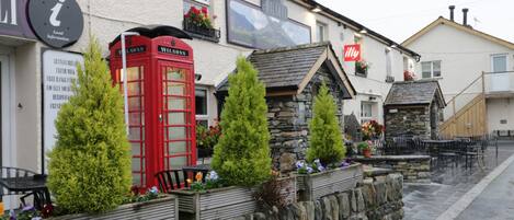 Un pub tradicional con una cabina telefónica roja, paredes de piedra y mesas al aire libre.