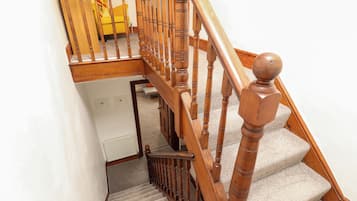 Una escalera de madera con barandilla, escalones alfombrados y un sillón amarillo al fondo.