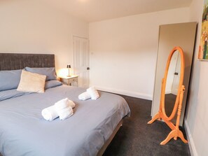 A hotel room with a bed, a bedside table with a lamp, a mirror, and a door. - 7 Lonsdale Terrace (Penrith)
