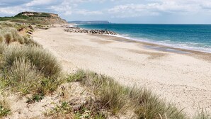 A beach with a rocky breakwater, grassy dunes, and a clear blue sky.
