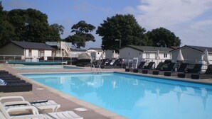 A swimming pool with lounge chairs and umbrellas, surrounded by mobile homes.