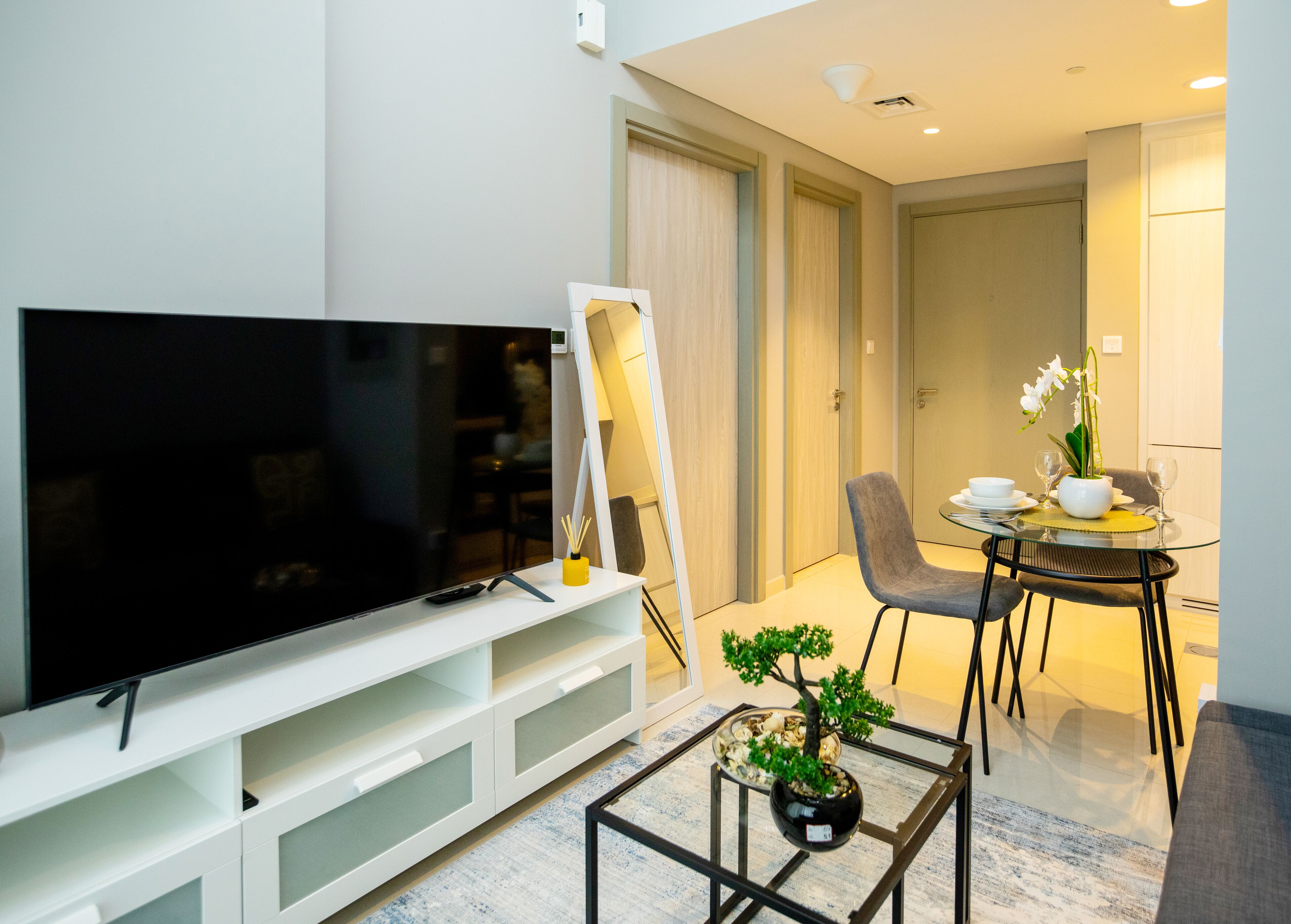 Ein modernes Wohnzimmer mit Flachbildfernseher, einem Esstisch mit Stühlen, einem kleinen Couchtisch mit Pflanze und einer weißen Unterhaltungseinheit.