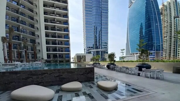 Un espacio exterior moderno con piscina, asientos y edificios altos al fondo.