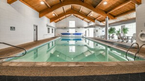 An indoor swimming pool with a wooden ceiling, clear glass walls, and a seating area with tables and chairs. - Quicksilver 1628 (Keystone)