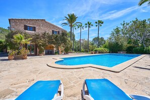 Una piscina con sillas de descanso, un edificio de piedra y palmeras.