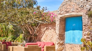 Un edificio rústico de piedra con una puerta azul, muebles de mimbre y árboles en flor.