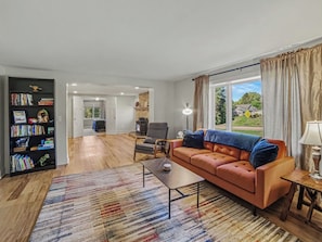 A living room with a sofa, a coffee table, a bookshelf, and a view of the outdoors.