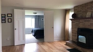 Una stanza con pavimento in legno, un caminetto e una porta che dà su un'altra stanza.