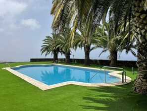 Relax by the pool surrounded by lush greenery and palm trees.