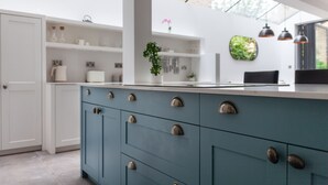 A modern kitchen with white and teal cabinetry, a central island, and a large window providing natural light. - 5 Bed Apartment in Clapham (London)