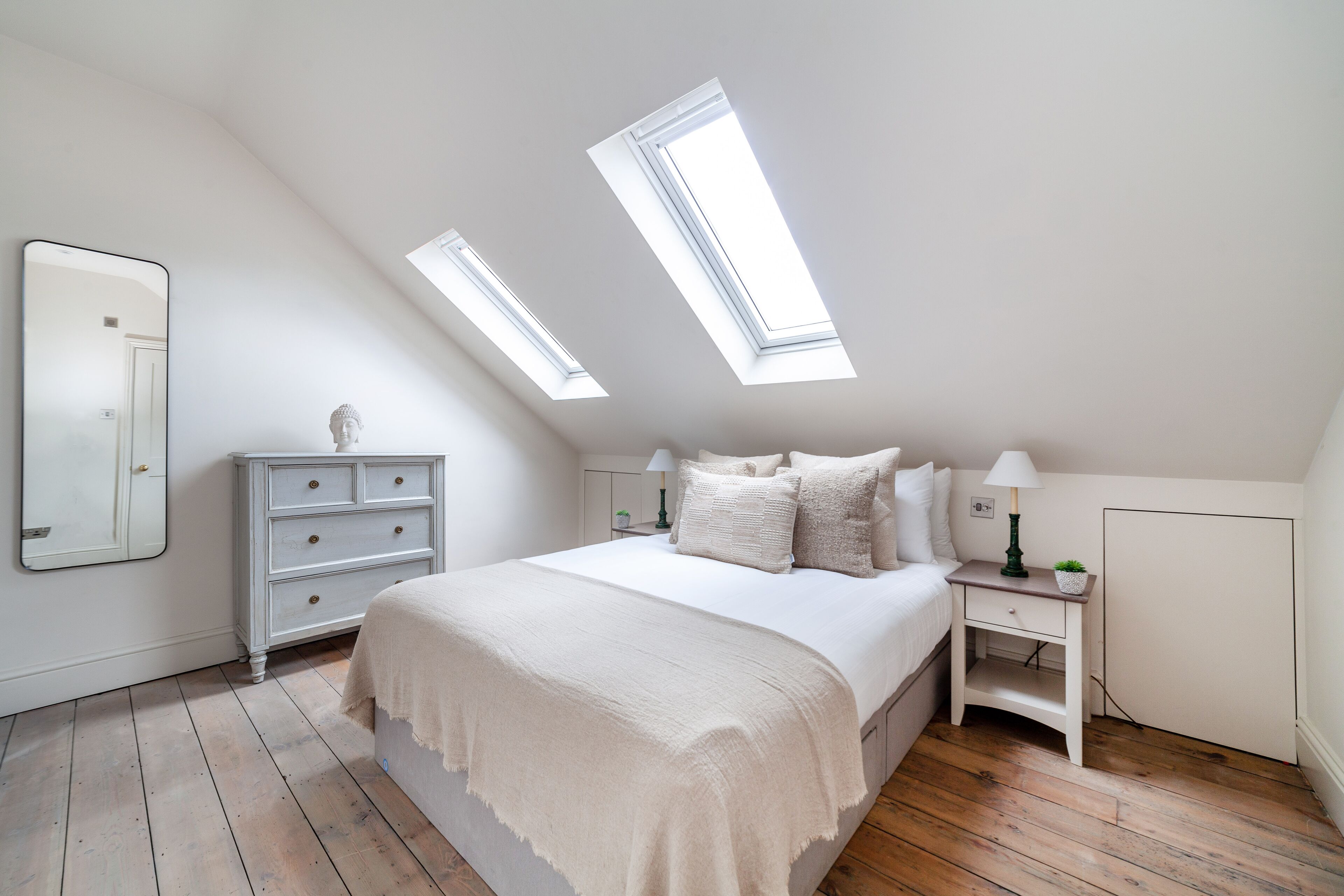 Een slaapkamer met een groot bed, twee nachtkastjes, een kapstok, een spiegel en dakramen.