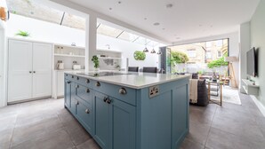 A modern kitchen with a large island, white cabinets, and a view to the outside. - 5 Bed Apartment in Clapham (London)