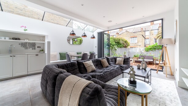 A modern living room with a sectional sofa, a glass coffee table, and a dining area with a table and chairs. - 5 Bed Apartment in Clapham (London)