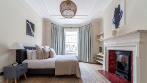 A bedroom with a bed, bedside table, lamp, and a fireplace. - 5 Bed Apartment in Clapham (London)