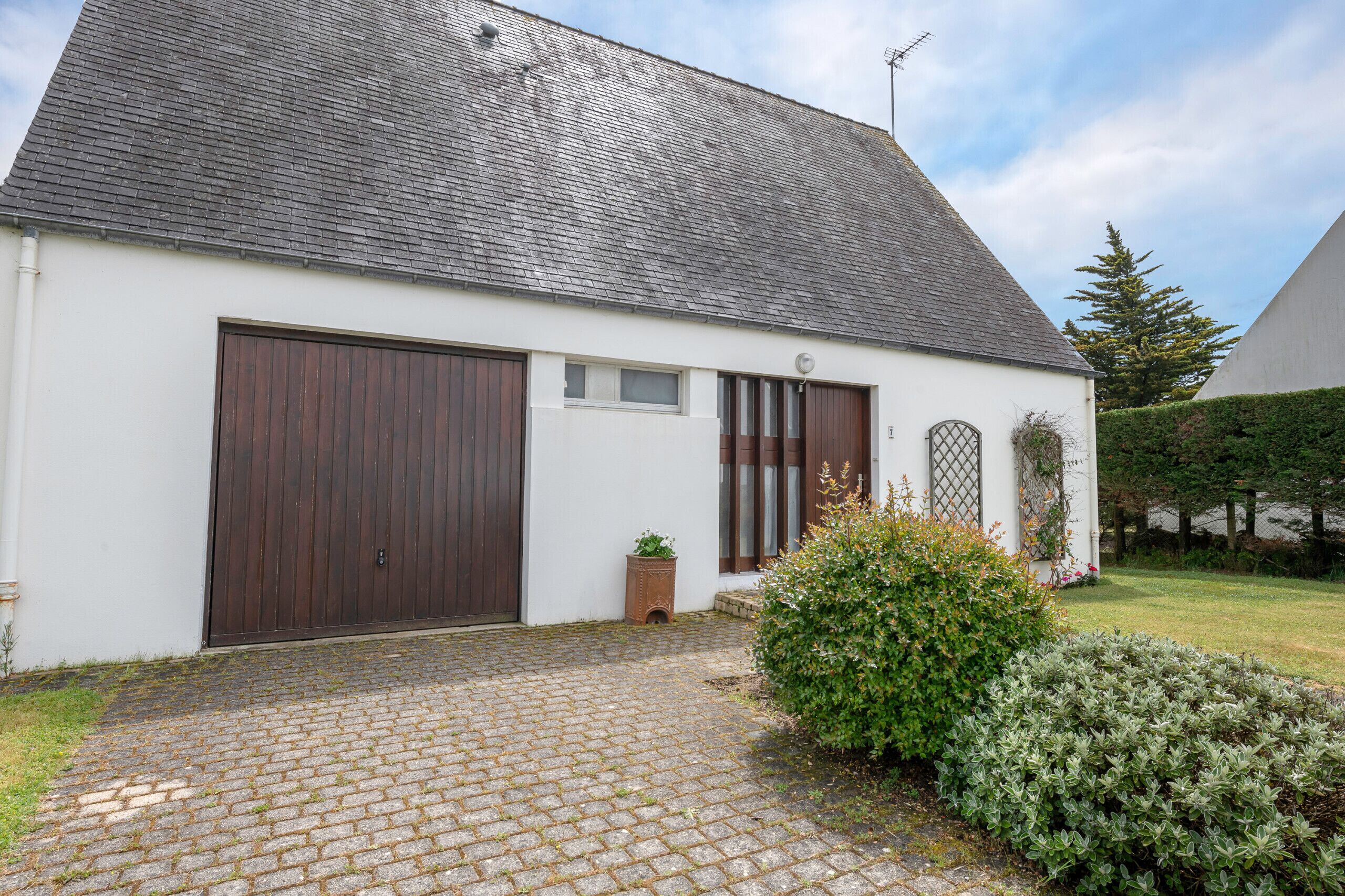 Ein eingeschossiges Haus mit einer dunkelbraunen Garagentür, einem kleinen Fenster und einer Satellitenschüssel auf dem Dach.