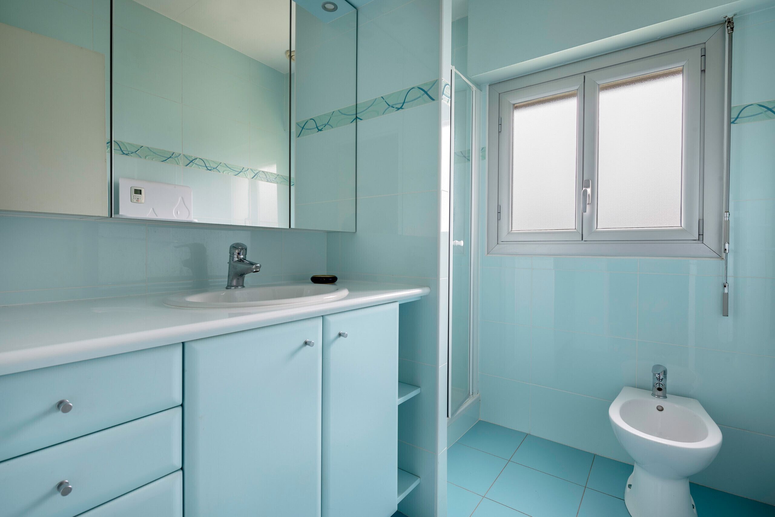 Ein Badezimmer mit weißem Waschbecken, einem Spiegel, einer Toilette und einem Fenster.