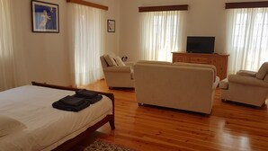 Habitació d'hotel amb un llit, dues butaques, un sofà, un moble de fusta i una televisió.