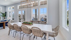 A spacious dining area with a long white table, wicker chairs, and a decorative centerpiece.