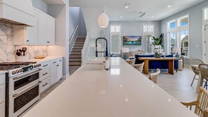 A modern kitchen with white cabinetry, a large island, and a dining area with a blue sofa and wicker chairs.