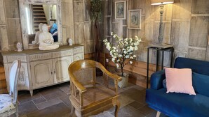 A room with a wooden cabinet, a blue sofa, a wooden chair, a floor lamp, and a small table with a vase of flowers. - Eco Gite Les Monts D'amara (CAMPUAC)