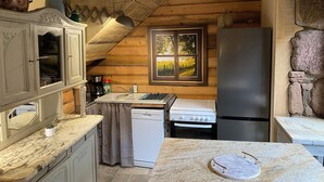 A rustic kitchen with wooden beams, a stone wall, a window with a view, a sink, a stove, and a refrigerator. - Eco Gite Les Monts D'amara (CAMPUAC)