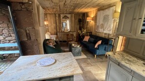 A rustic interior with a stone wall, a wooden ceiling, a blue sofa, a marble countertop, and a dining area with a table and chairs. - Eco Gite Les Monts D'amara (CAMPUAC)